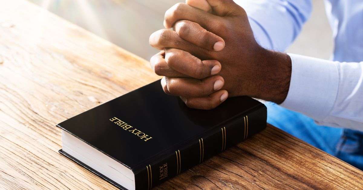 a man's hands in praying position on top of Bible